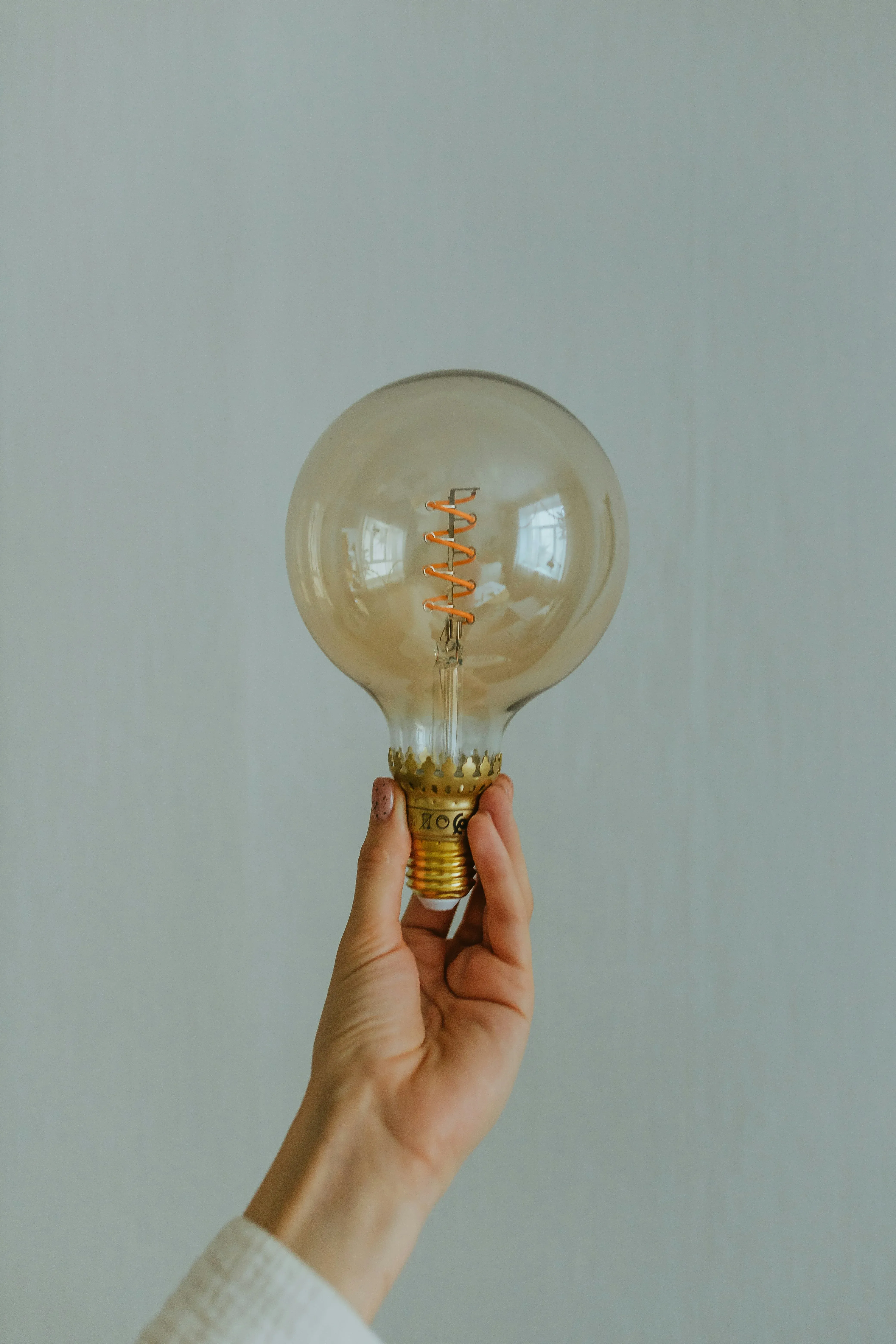 A hand holding a filament bulb against a pale wall